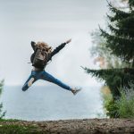woman jumping wearing green backpack