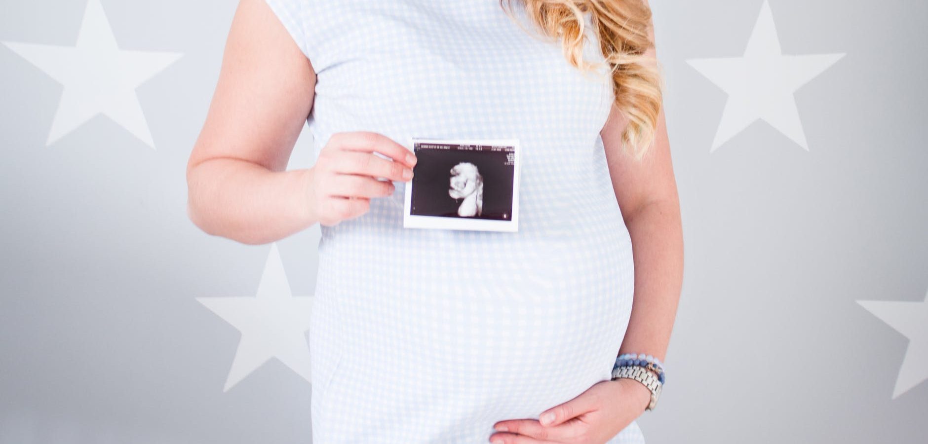 woman wearing white cap sleeved dress holding ultrasound result photo