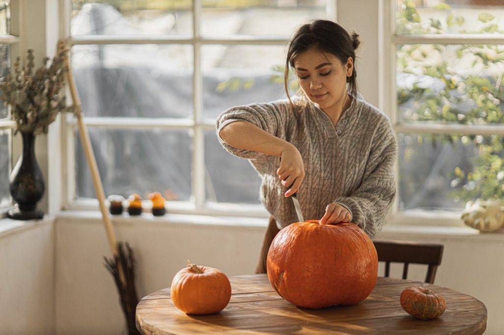 woman in gray sweater carving orange pumpkin