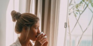 blond woman drinking coffee and looking through window
