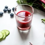 red juice in a glass beside cucumber and beetroot