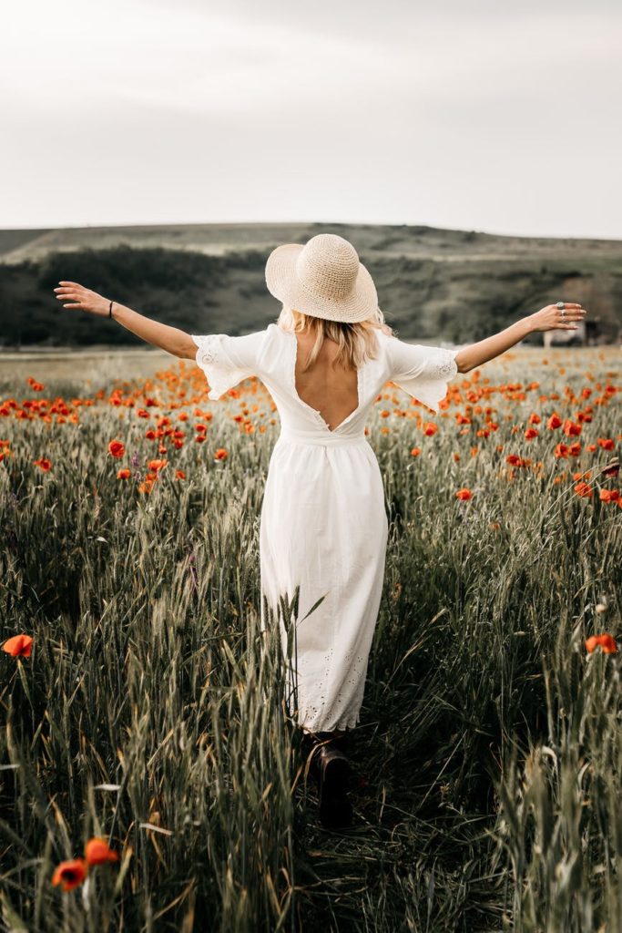 elegant woman in hat walking in field with flowers